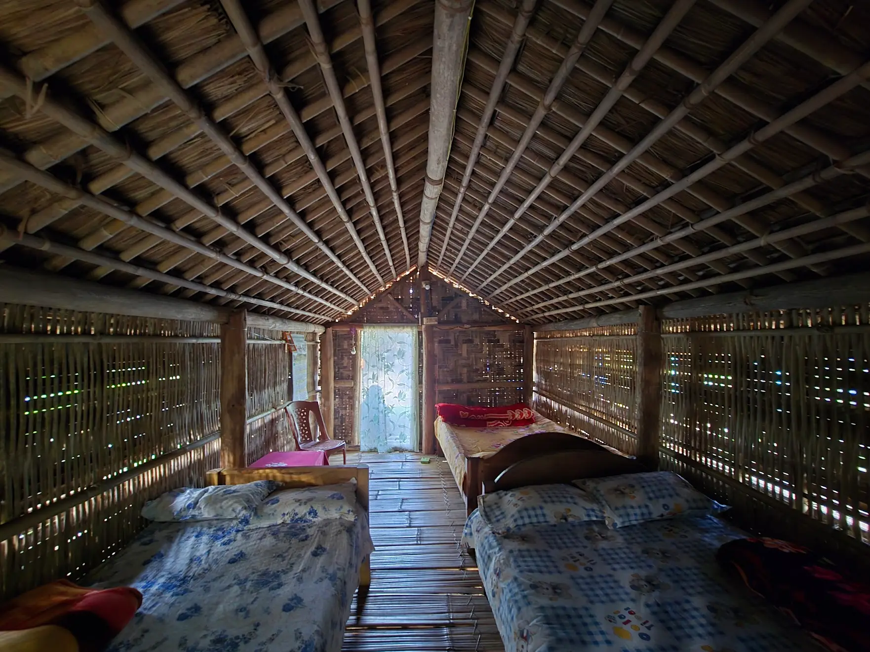 Interior of a rustic bamboo hut with beds along both sides and light entering through the doorway.